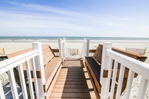 Eine Holzterrasse führt zu einem Strand, mit weißen Geländern.