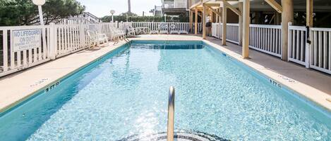 A swimming pool with a no lifeguard sign, surrounded by a white fence and lounge chairs.