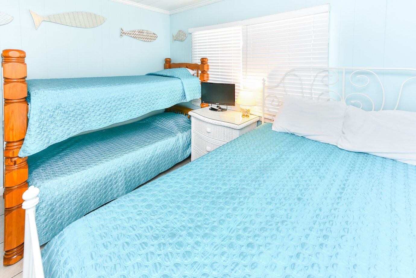 A room with three bunk beds, a small white dresser, a television, and a window with blinds.