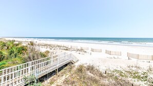 Ein Strand mit einer Holzpromenade, die zum Ufer führt, Sanddünen und dem Meer.