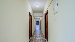 A hallway with a tiled floor, wooden doors, and a light fixture on the ceiling. - Urban Drift by Urban Hotels (Bengaluru)
