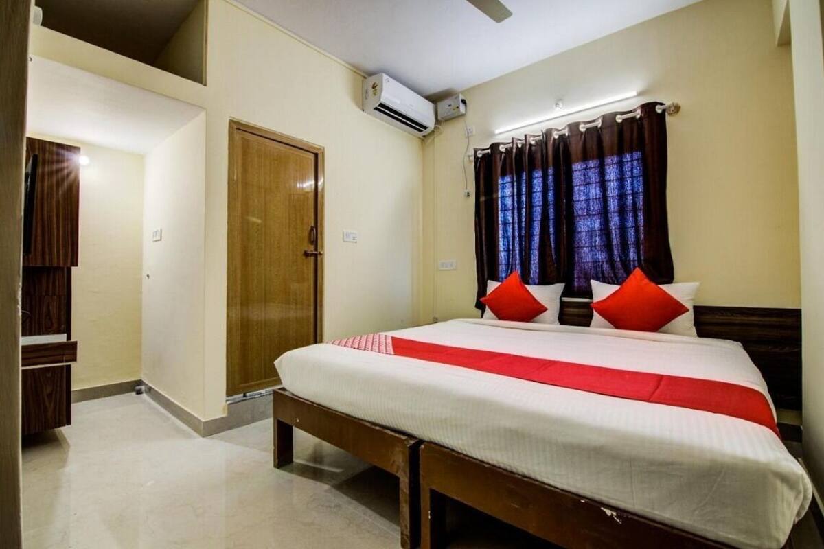 Een hotelkamer met een bed, een houten deur, een airconditioning en een raam met gordijnen.