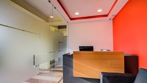 A modern reception area with a wooden desk, a black chair, and a red accent wall. - Urban Drift by Urban Hotels (Bengaluru)