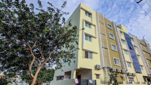 A multi-story residential building with a flat facade, a gated entrance, and a small tree in the foreground. - Urban Drift by Urban Hotels (Bengaluru)