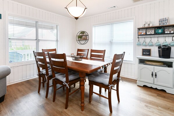 A dining area with a wooden table and chairs, a hanging light fixture, and a white cabinet with shelves.