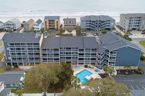 A multi-story hotel with a pool, located near a beach.
