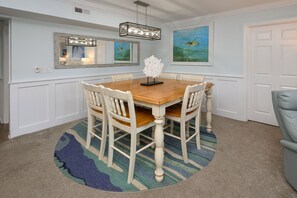 A dining room with a wooden table and white chairs, a rug, and two paintings on the wall.