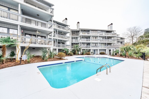 A multi-story hotel with a swimming pool, balconies, and outdoor plants.