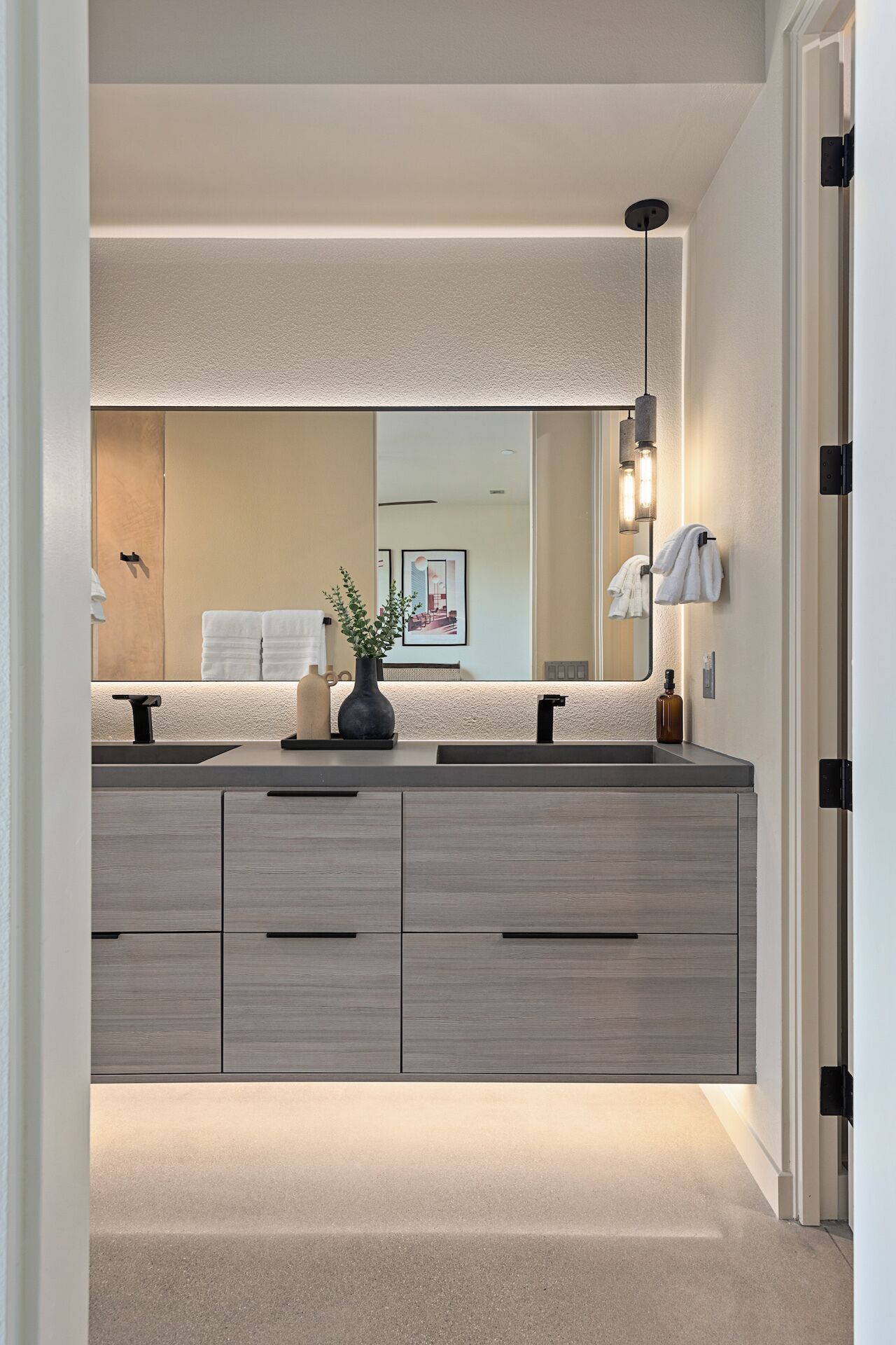 Un baño moderno con tocador doble, un espejo grande y una planta en maceta.
