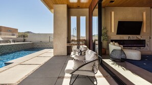 Ein moderner Außenbereich mit Pool, Grill und einer gemütlichen Lounge mit Fernseher und Kamin.