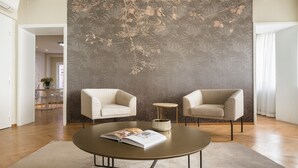 A modern living room with two beige armchairs, a round coffee table, and a decorative wall with a floral pattern.