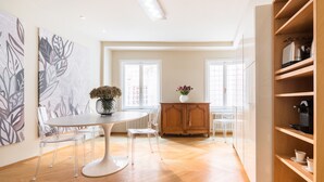 A modern kitchen with a dining area, featuring a round table, clear chairs, a wooden cabinet, and a radiator.
