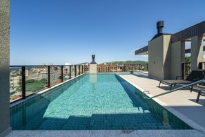A rooftop pool with clear blue water, surrounded by a tiled deck and a view of the cityscape. - 1034 - Apartamento com piscina apto 104 (Bombinhas)