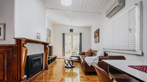 A spacious living room with a fireplace, a sofa, a dining table, and a large window with blinds.