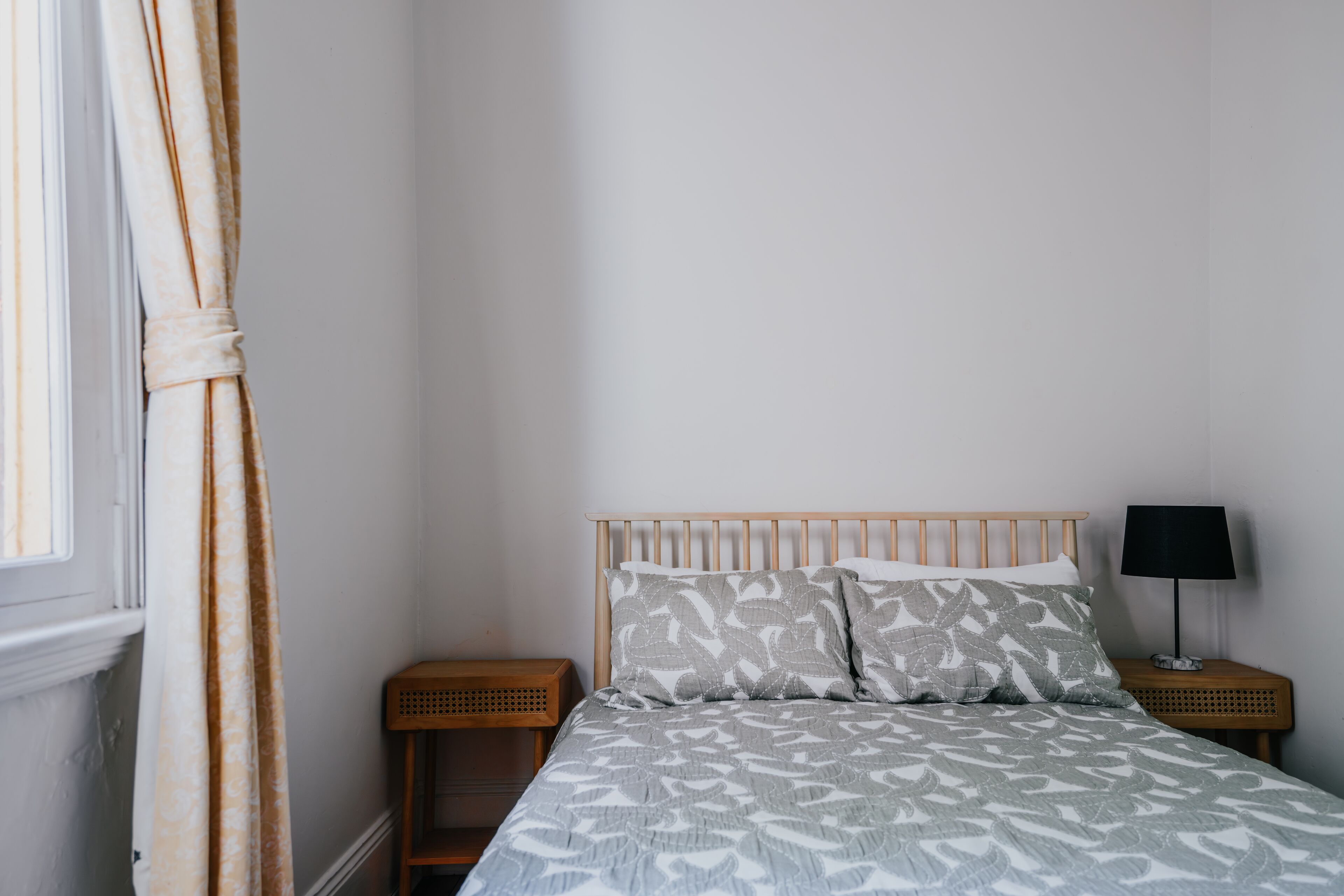Une chambre à coucher avec un lit, une table de chevet, une lampe et une fenêtre avec des rideaux.