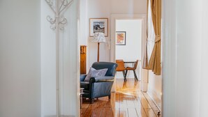 A room with a wooden floor, a black leather chair with a pillow, a table with chairs, and a lamp.