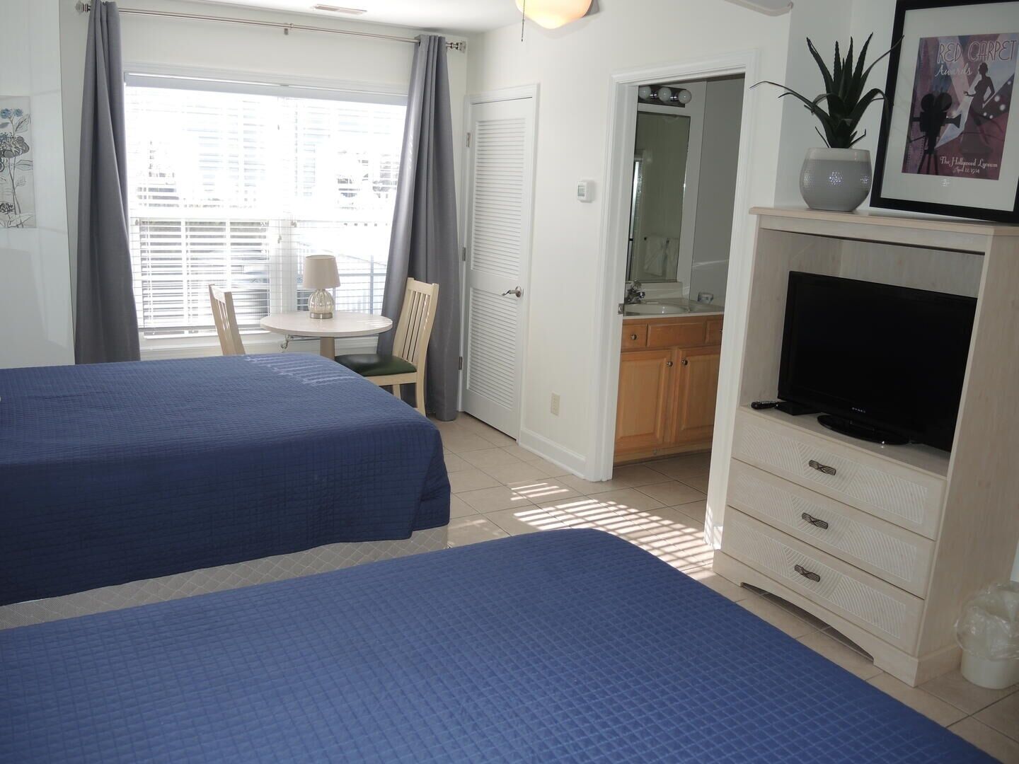 Een hotelkamer met twee bedden, een televisie, een tafeltje met een lamp, een plant en een lijstje aan de muur.