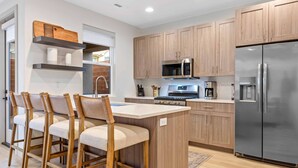 A modern kitchen with wooden cabinets, a stainless steel refrigerator, a microwave, and a central island with bar stools. - Fairway Getaway #55 3 Bedroom Townhouse (Santa Clara)