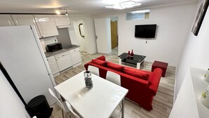 Een compacte leefruimte met kitchenette, een eethoek met een rode bank en een aan de muur bevestigde televisie.