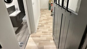 Een hal met modern design, met een houten vloer, een deur met metalen rooster en een spiegel aan de muur.
