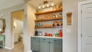 Una cocina con armarios de madera, una encimera con varios utensilios de cocina y un estante en la pared con objetos decorativos.