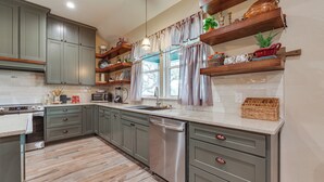 Una cocina moderna con armarios grises, lavavajillas de acero inoxidable y estantes de madera.