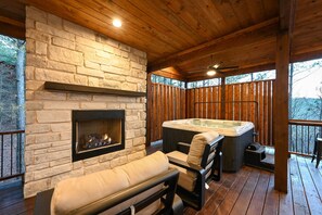 A wooden deck with a stone fireplace, a hot tub, and outdoor seating. - Luxe Group Getaway w/ 2-story Deck in Broken Bow! (Broken Bow)