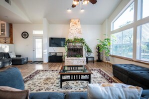 A living room with a stone fireplace, a sofa, a coffee table, and a television. - Private Luxury Getaway Fire Pit Near Weddings (Dripping Springs)