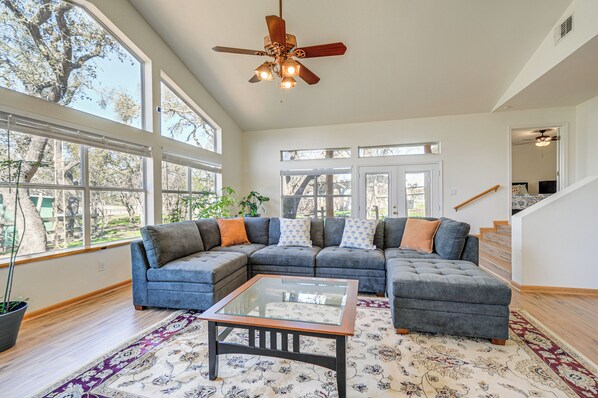 A spacious living room with a large sectional sofa, a glass coffee table, and a ceiling fan. - Hill Country Retreat Near Wineries & Weddings! (Dripping Springs)