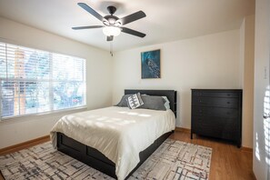 Une chambre à coucher avec un lit, un ventilateur de plafond, une commode et une fenêtre avec des stores.