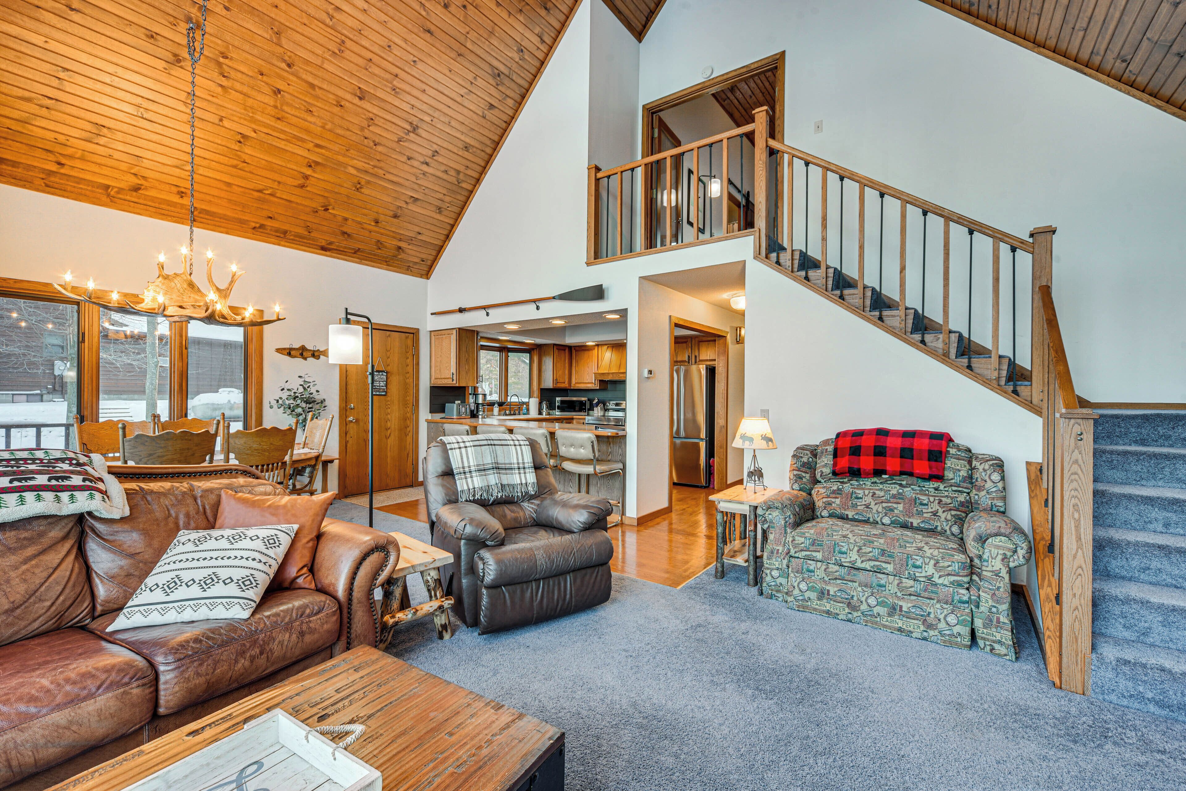 A spacious living room with a high ceiling, a staircase, and a kitchen area.