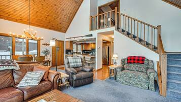 A spacious living room with a high ceiling, a staircase, and a kitchen area.