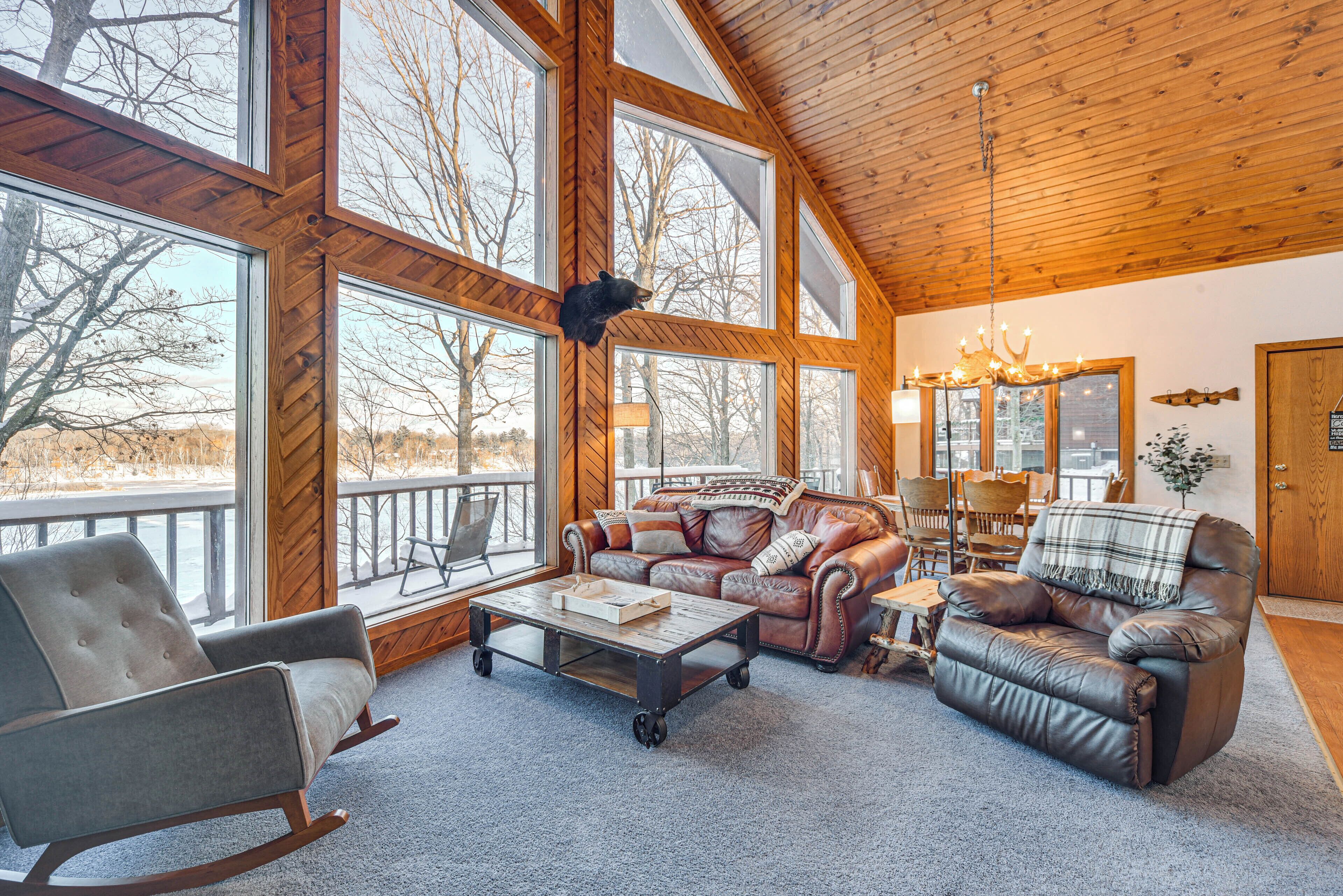 A cozy living room with a leather sofa, a rocking chair, and a coffee table. Large windows offer a view of the outdoors.