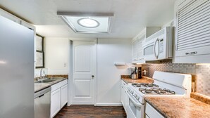 A narrow kitchen with white cabinets, a stainless steel refrigerator, a gas stove, and a microwave. - Fort Walton Home w/ Shared Pool - 2 Mi to Beach! (Fort Walton Beach)