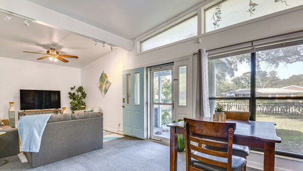 A living room with a sofa, a TV, a ceiling fan, and a large window with a view of the outdoors. - Fort Walton Home w/ Shared Pool - 2 Mi to Beach! (Fort Walton Beach)