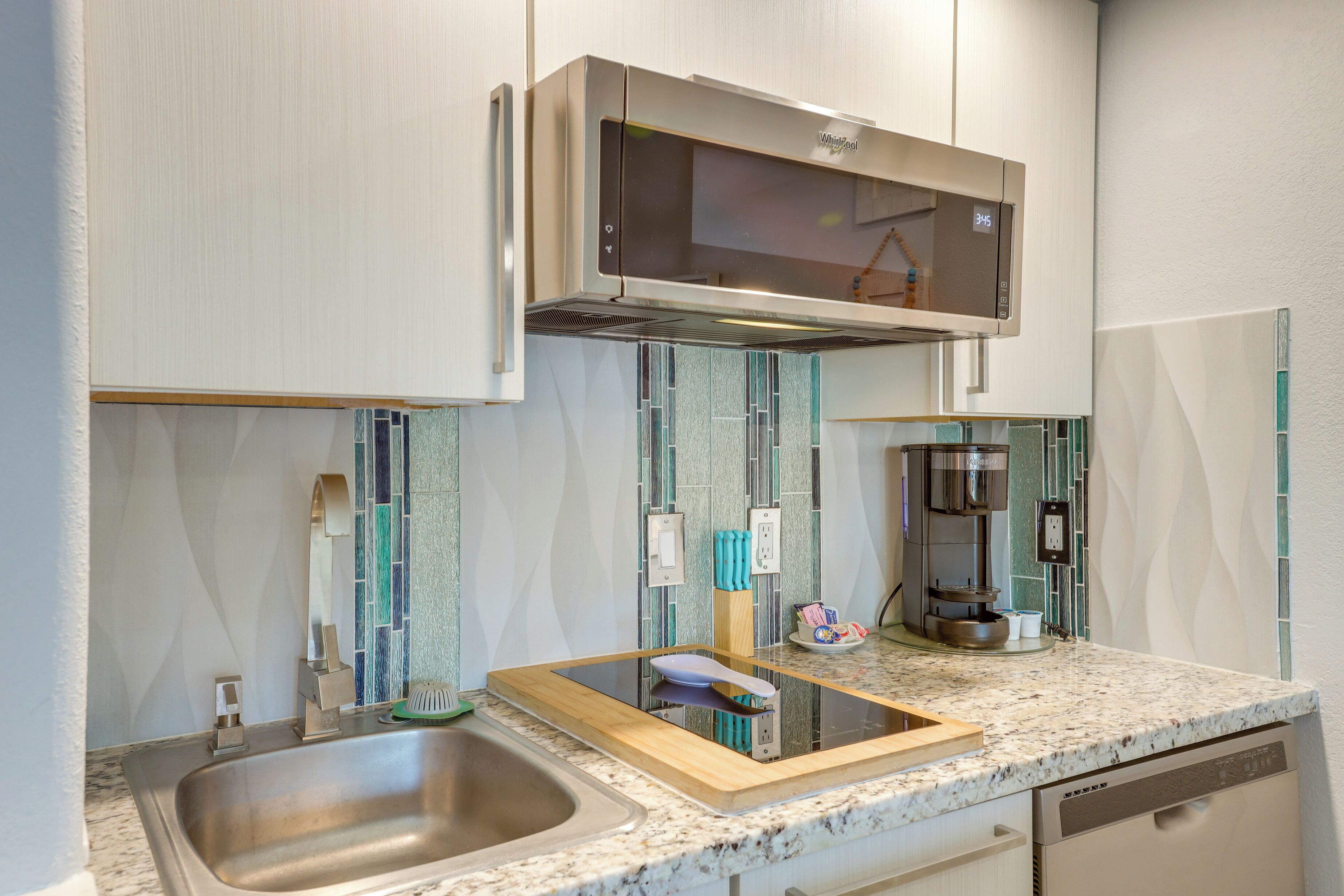 A modern kitchen with a stainless steel sink, a built-in microwave, and a coffee maker.