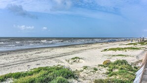 Une plage avec un rivage sablonneux, des dunes herbeuses et un ciel dégagé.