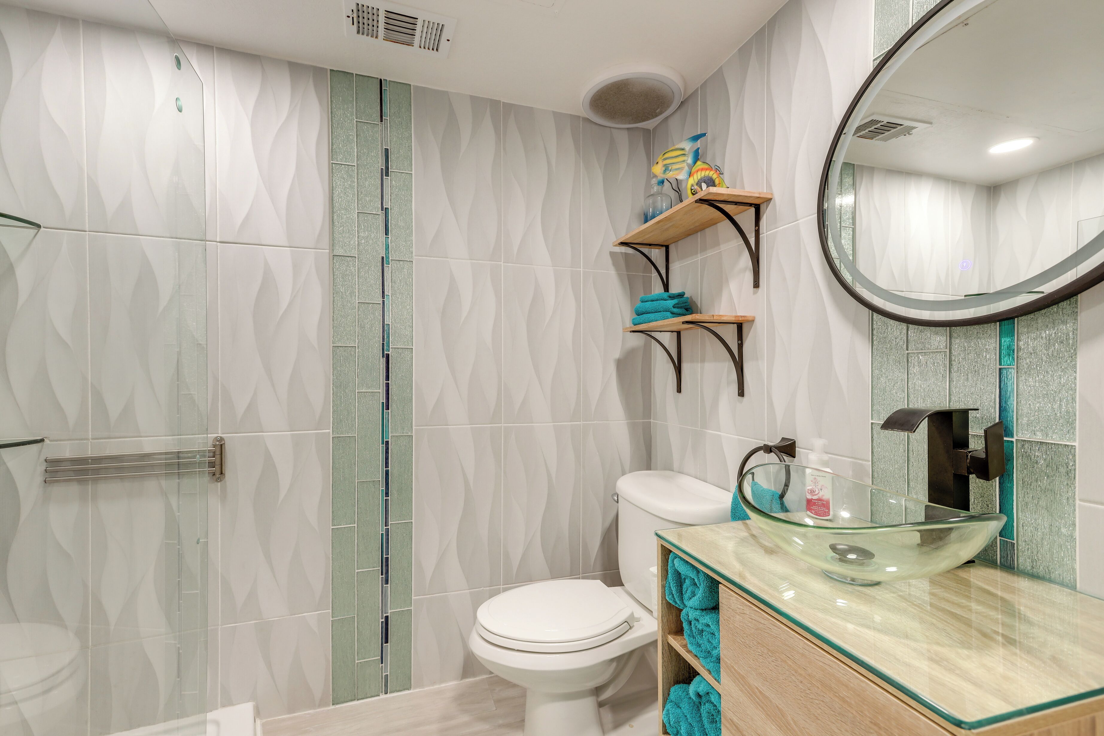 A modern bathroom with a glass vessel sink, a toilet, and a shower area.