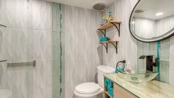 A modern bathroom with a glass vessel sink, a toilet, and a shower area.