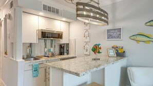 Une cuisine moderne dotée d’un plan de travail en marbre, d’appareils électroménagers en acier inoxydable et d’un luminaire suspendu.