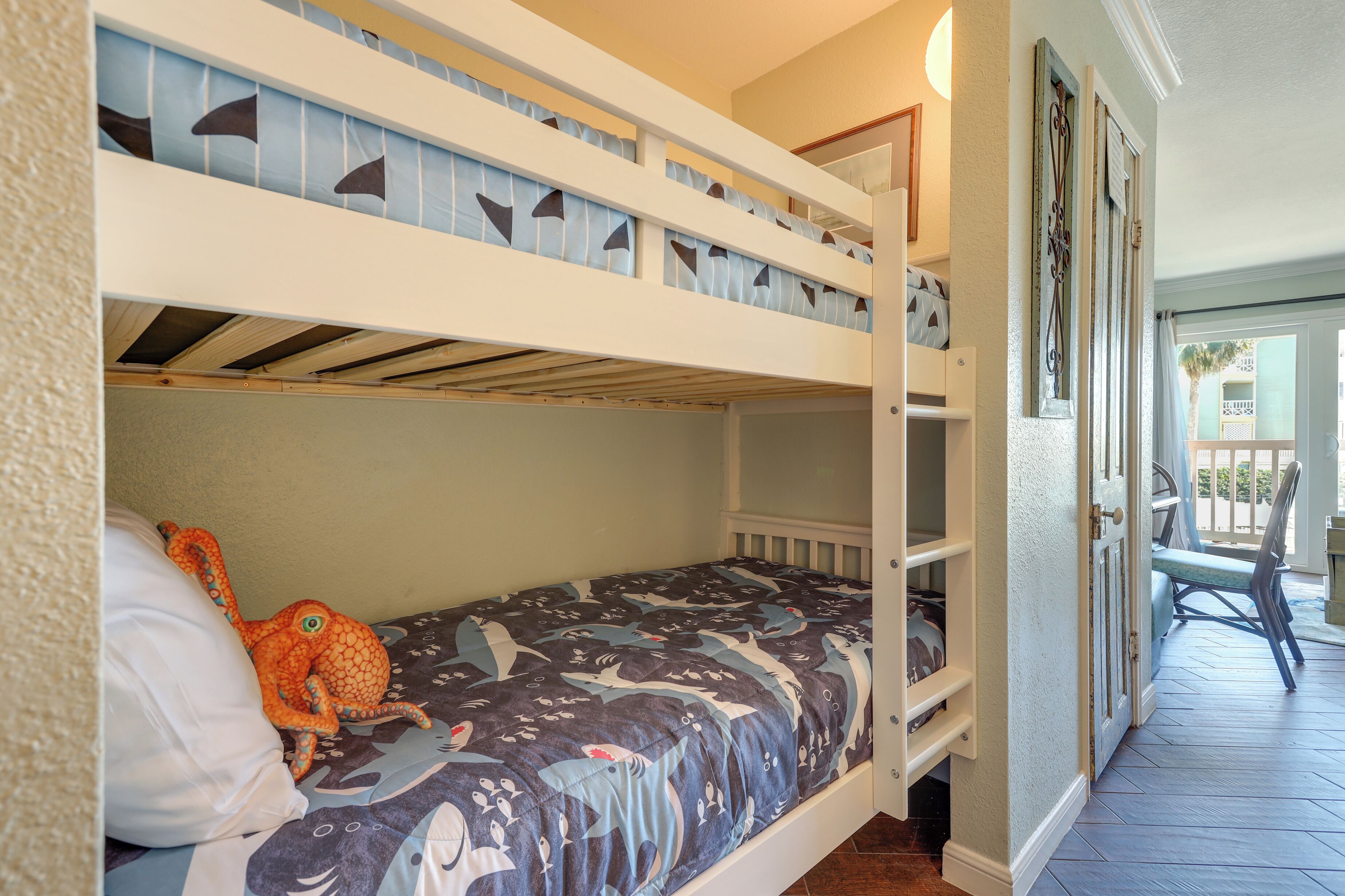 A bunk bed with a shark-themed bedspread, a plush octopus toy, and a white crib on the lower bunk.