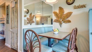 Un coin repas avec une table en bois, un banc rembourré bleu et deux chaises en bois. Un bol de collations est posé sur la table.