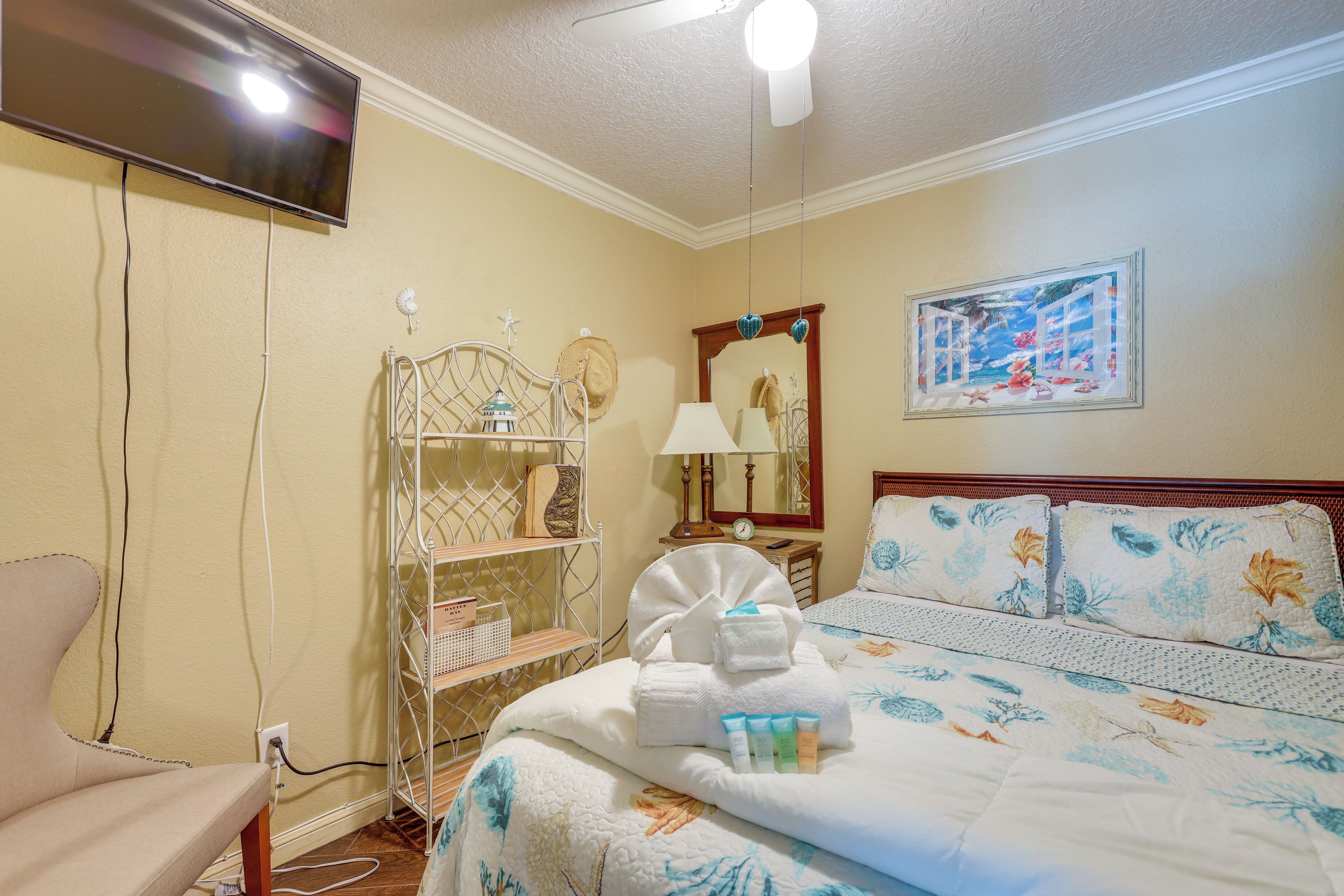 A hotel room with a bed, a chair, a TV, a shelf with toiletries, and a painting on the wall.