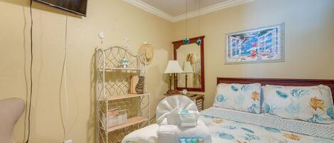 A hotel room with a bed, a chair, a TV, a shelf with toiletries, and a painting on the wall.