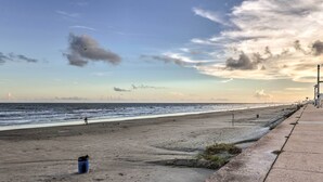 Une plage avec une promenade en béton, une poubelle et l’océan en arrière-plan.