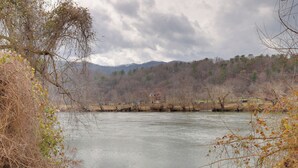Une rivière avec une maison sur la rive opposée, entourée d’arbres et de collines.