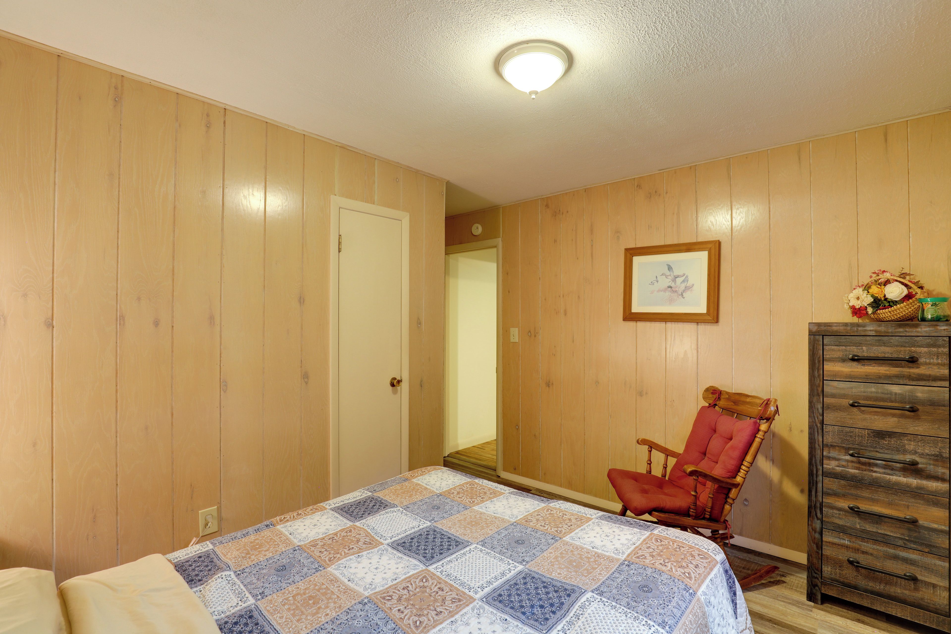 Une chambre avec des murs en bois, une couvre-lit matelassée, une commode en bois et une chaise.
