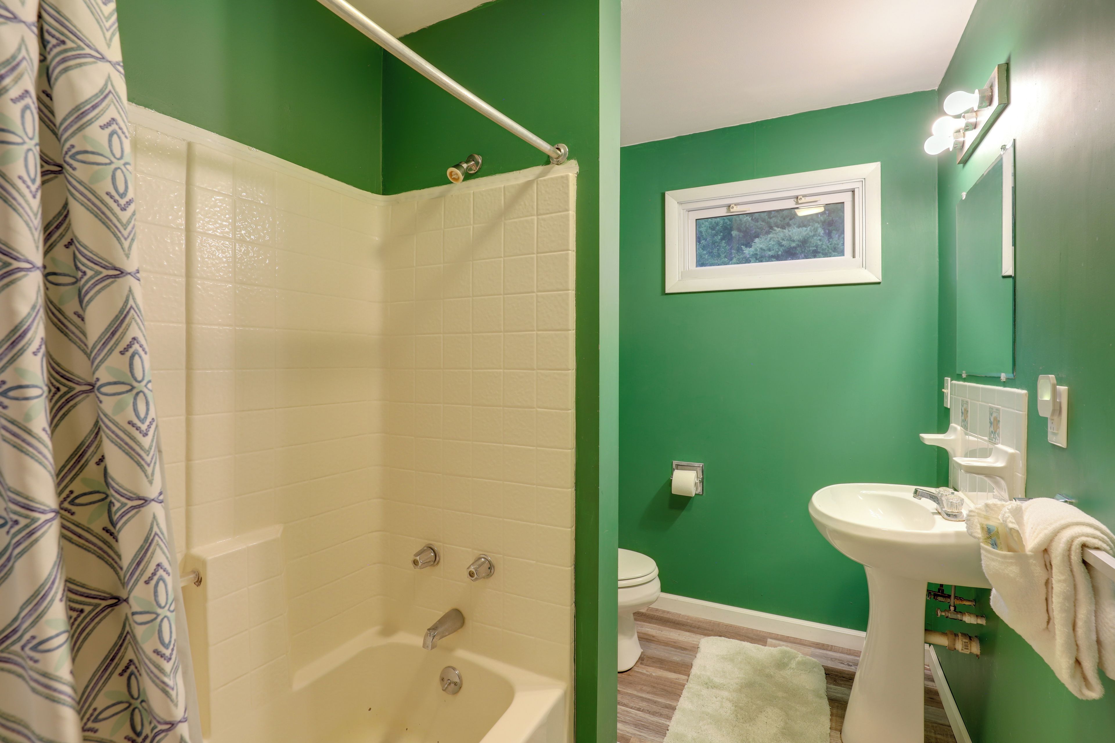 Une salle de bain avec un mur vert, une baignoire blanche, un lavabo blanc et des toilettes blanches.