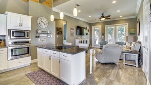 A modern kitchen with white cabinetry, a central island, and a dining area with a gray sofa and a small table. - Walk to Beach: Stunning Gulfport Getaway (Gulfport)