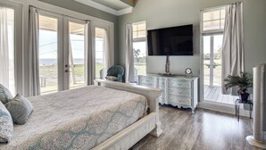 A bedroom with a large bed, a TV, a dresser, and a view of the outdoors. - Walk to Beach: Stunning Gulfport Getaway (Gulfport)